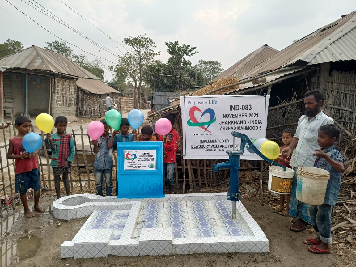 Children and adults around a newly installed water pump with a banner in a rural setting.