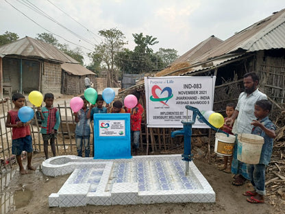 Children and adults around a newly installed water pump with a banner in a rural setting.