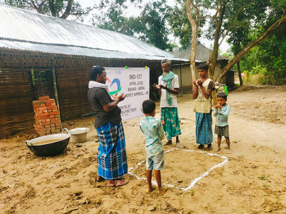 People standing outdoors with a banner and children making dua and prayer in a rural setting