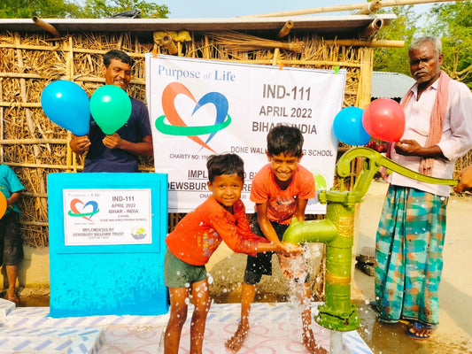 Children playing with a water pump in front of a banner with 'Purpose a Life' branding.
