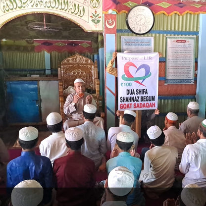 Group of people in a mosque with a speaker addressing them, surrounded by religious posters and decorations.