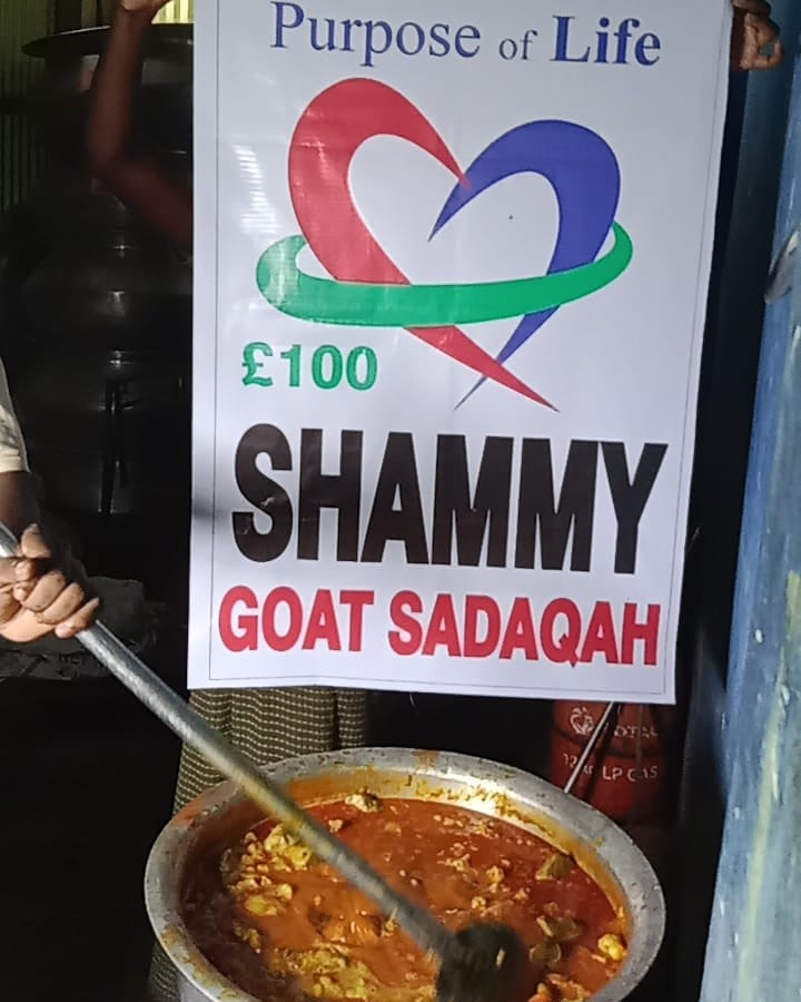 Person holding a sign for 'Shammy Goat Sadaqah' with a pot of food in the foreground.
