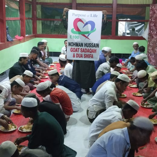 Group of people sitting for a meal in a communal dining area with a banner in the background.