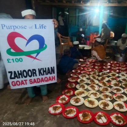 Person holding a sign with 'Purpose of Life' and 'Zahoor Khan Goat Sadaqah' text, surrounded by plates of food.