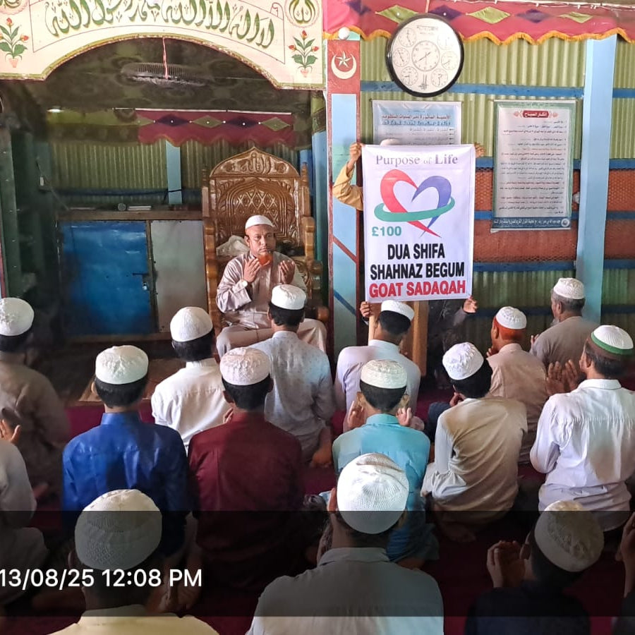 Group of people in a mosque with a speaker addressing them, surrounded by religious posters and decorations.